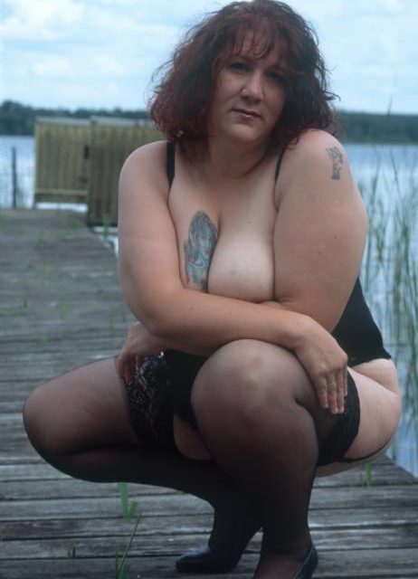 Dicke Frau mit tätowierten Brüsten posiert frivol auf einem Steg